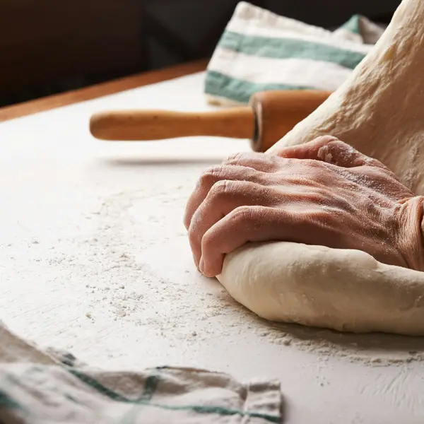 Mjöliga händer knådar deg bredvid en kavel